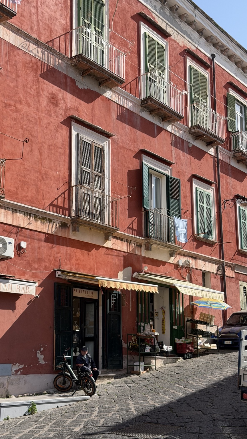 Botteghe e balconi di un palazzo rosso lungo una strada lastricata