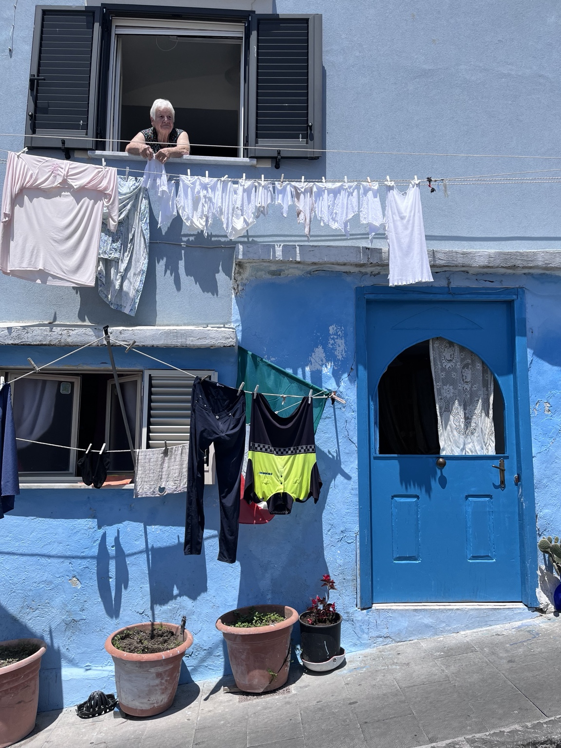 Una donna alla finestra di una casa azzurra, con il bucato steso